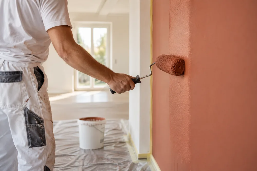 Maler trägt mit einer Farbrolle einen warmen Terrakottaton auf eine Innenwand auf.